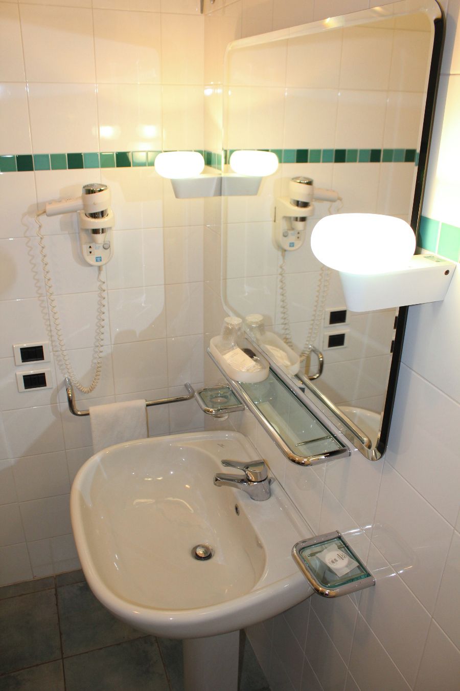 A bathroom with a sink, mirror, towel rack, and two wall-mounted hair dryers.