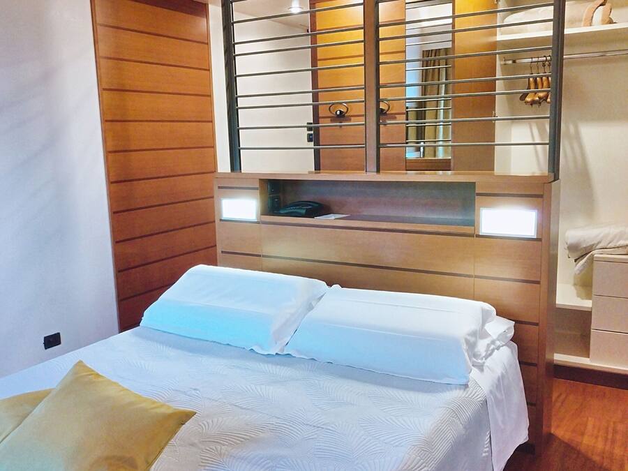 A hotel room with a bed, a wooden wardrobe, and a mirror above the bed.