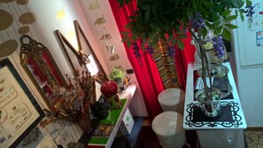 Una habitación con una mesa verde, cortinas rojas y una planta con flores moradas.