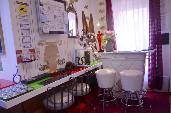 Una cocina con encimera blanca, dos taburetes blancos y una ventana con cortinas rojas.