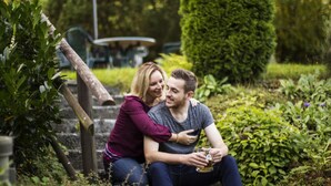 Una pareja sentada sobre escalones de piedra en un jardín, con un pabellón al fondo.