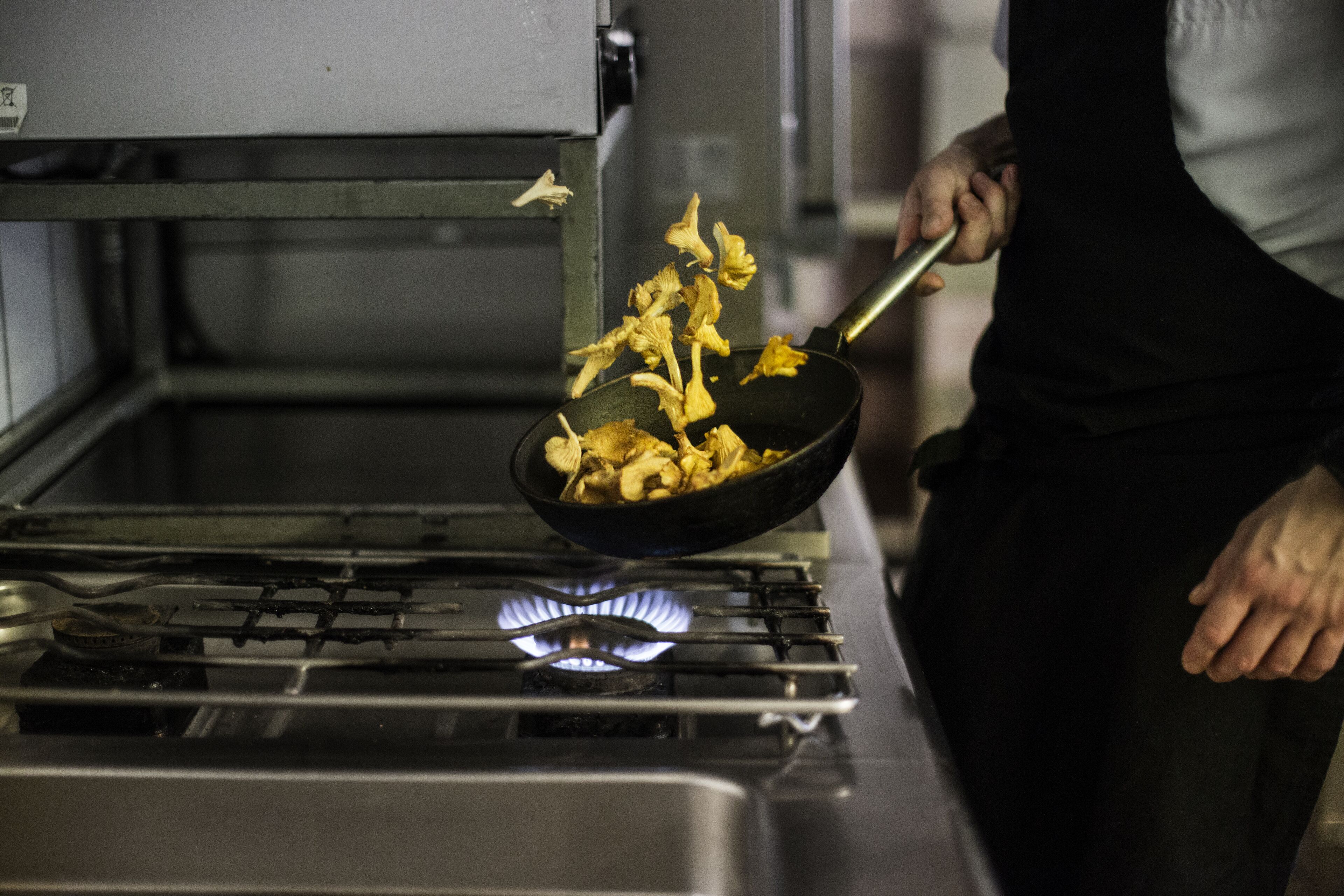 A person cooking mushrooms in a pan on a stove.