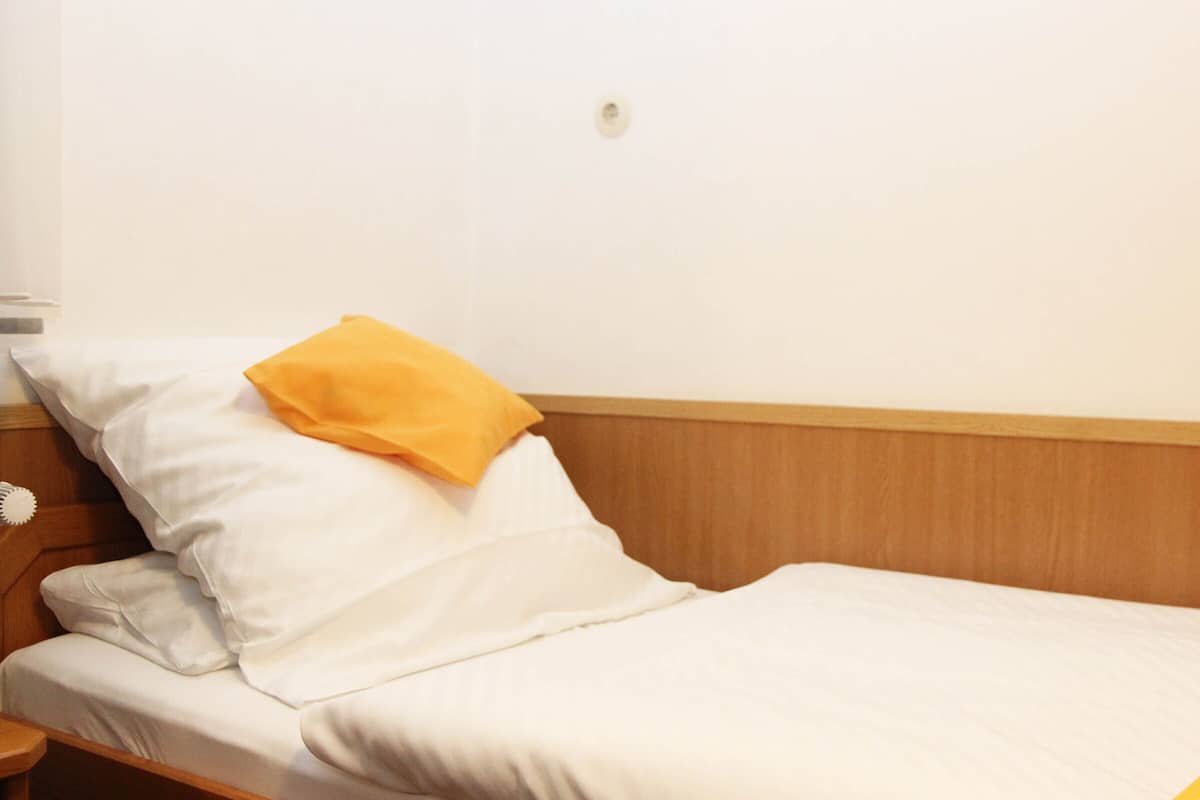 Cama bem arrumada com roupa de cama branca e um único travesseiro amarelo.