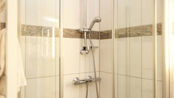 Une douche équipée d’un pommeau de douche à main et d’un pommeau de douche fixe fixé au mur, tous deux dotés de finitions chromées.