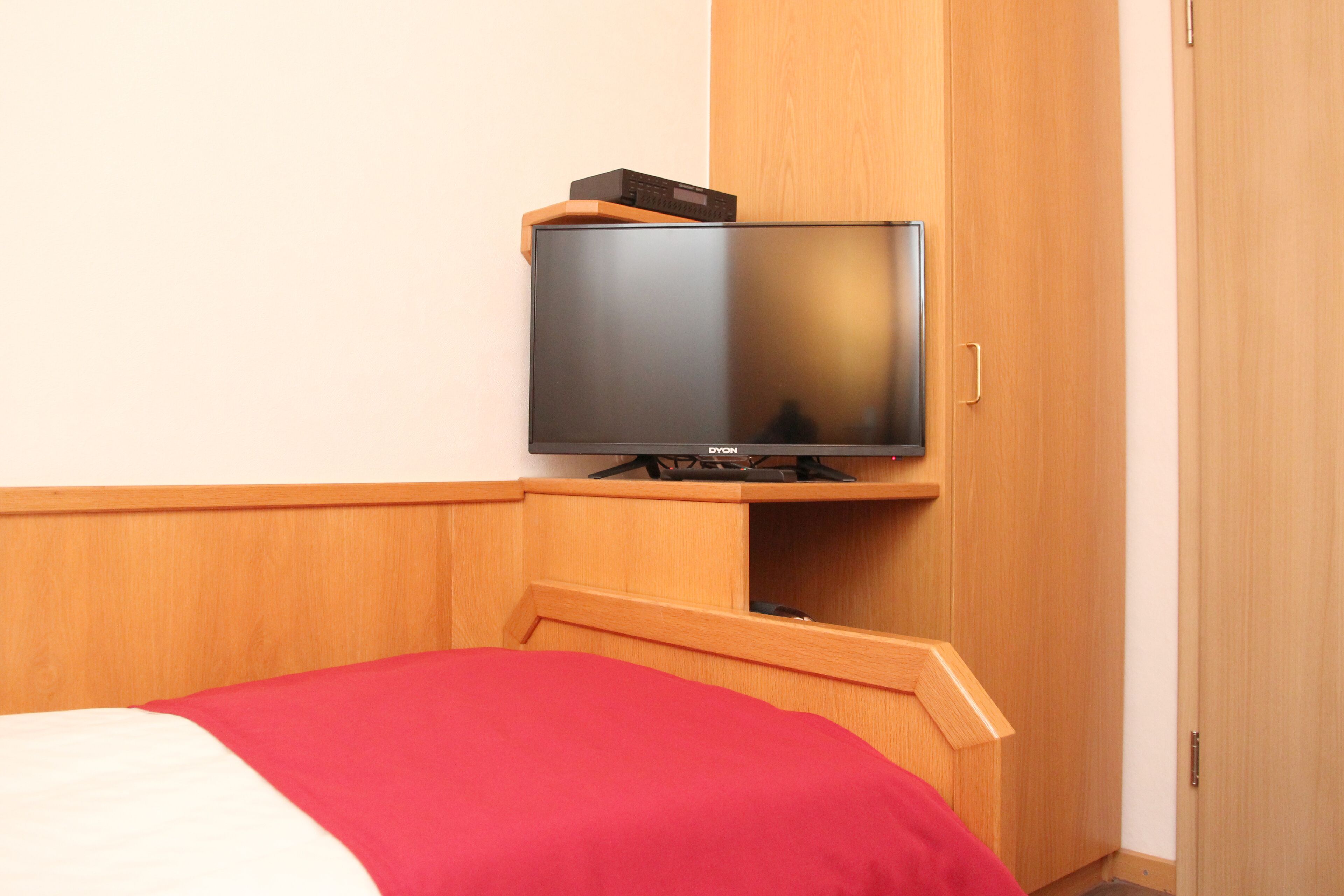 Ein Hotelzimmer mit Bett, Fernseher auf einem Holzständer und einem Holzschrank.