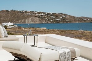 Un espace extérieur ensoleillé, aménagé avec des sièges, offrant une vue sur la mer et une colline.