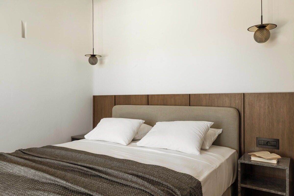 A neatly made bed with two pillows, a wooden headboard, and a bedside table with a book.