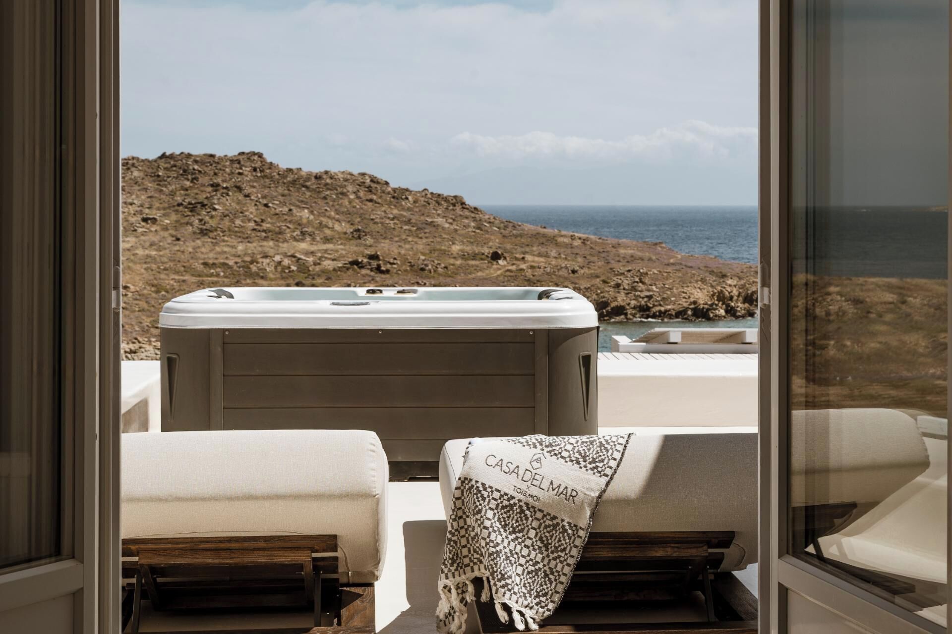 A cozy outdoor seating area with a hot tub, a bench, and a view of the sea and rocky landscape.