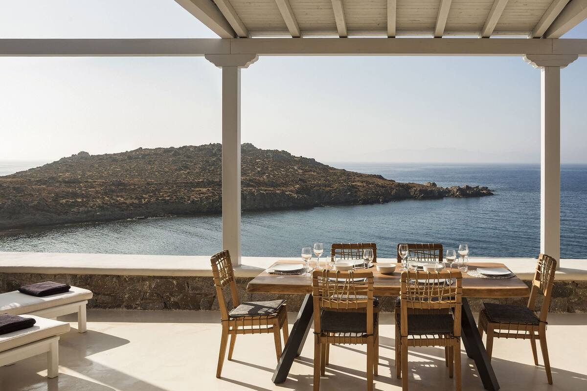 Une terrasse avec une table dressée pour le dîner, offrant une vue sur une côte rocheuse et la mer.