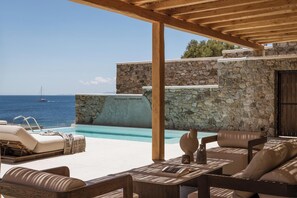 Un espace aménagé au bord de la piscine, avec des murs en pierre, du mobilier d’extérieur et une vue sur la mer.