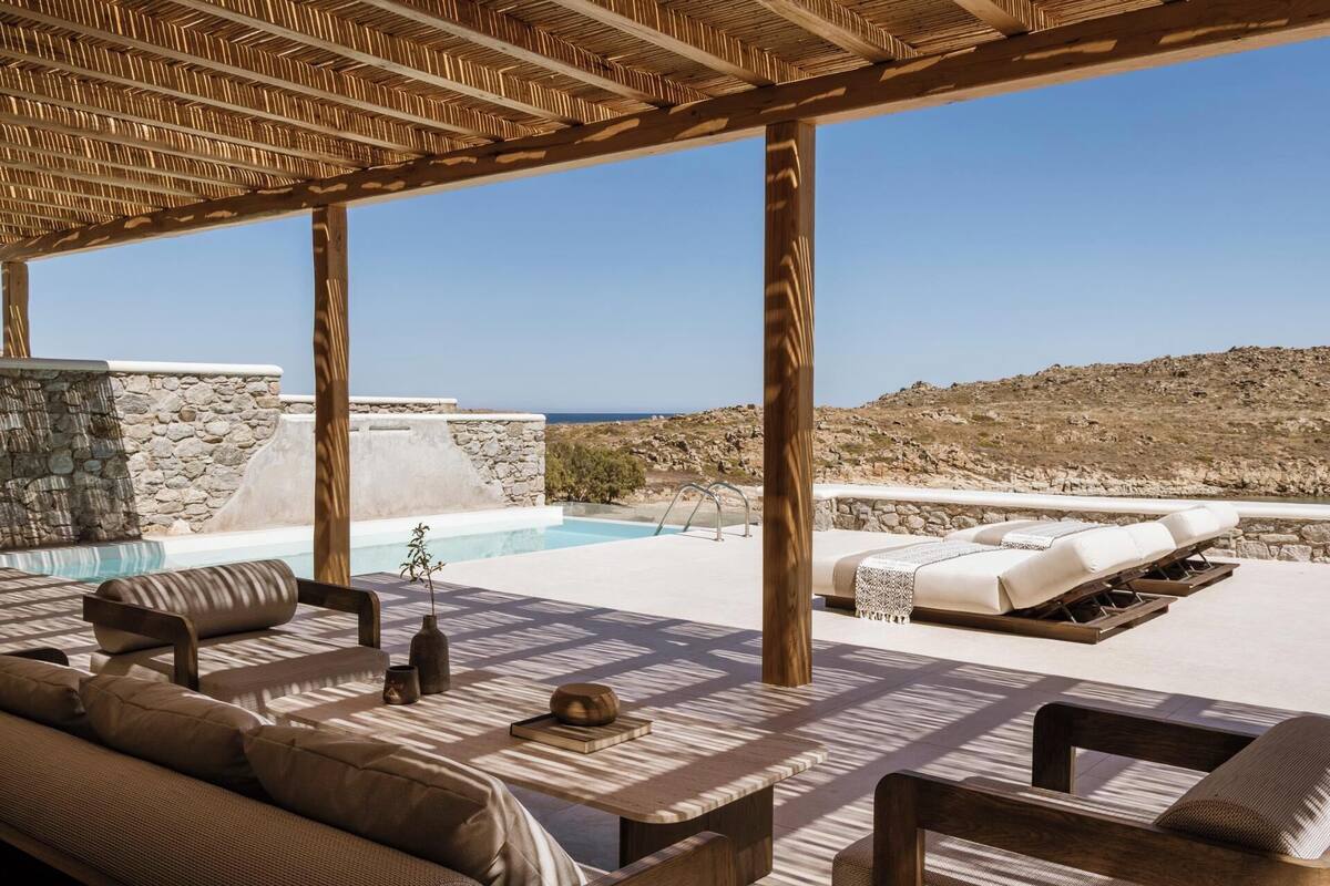 Un espace de détente extérieur baigné de soleil, avec une piscine, des murs en pierre et une vue sur la mer.