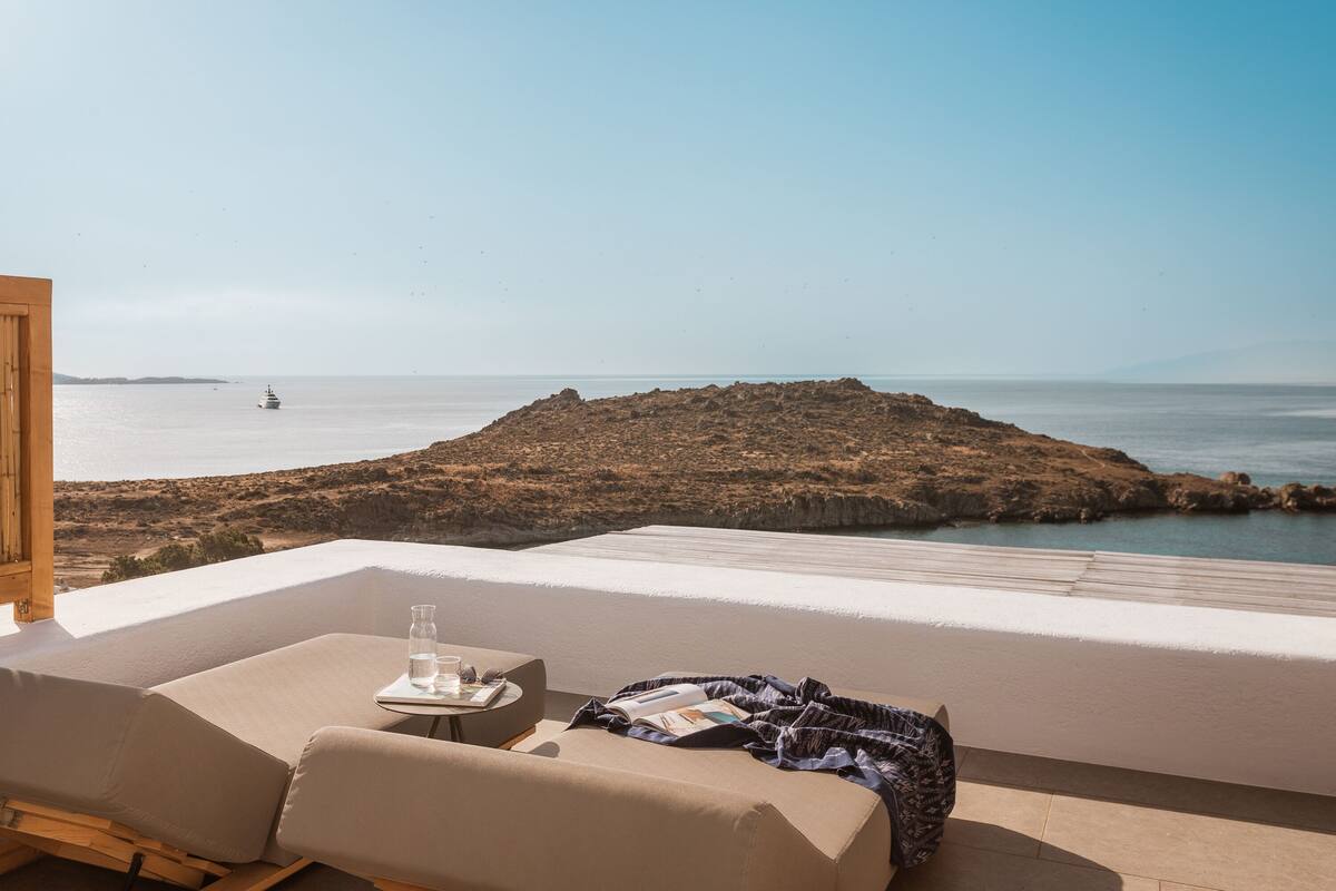 Un balcon avec vue sur la mer, un bateau à l’horizon et une île rocheuse.
