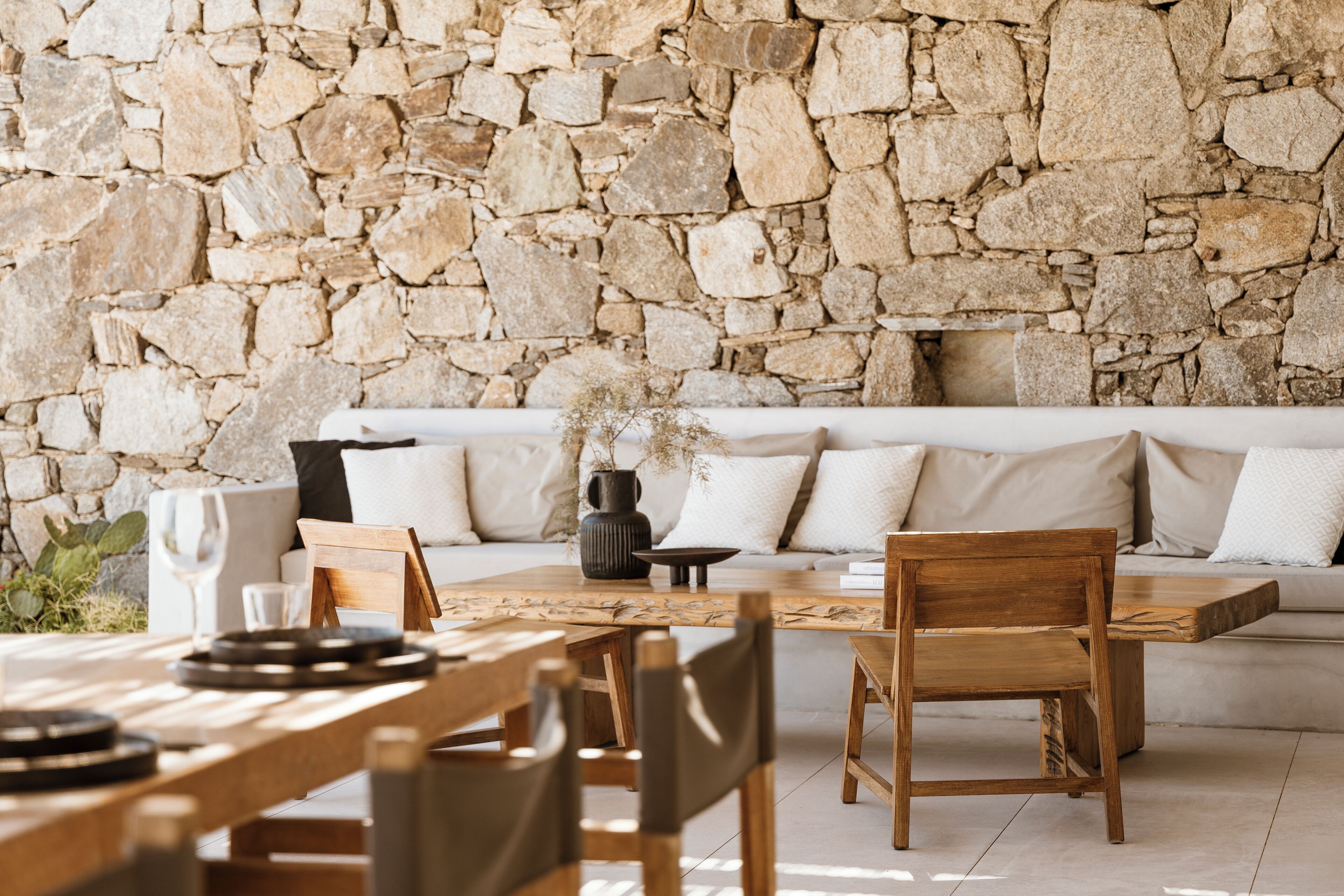 A stone wall, wooden furniture, and a white sofa in a dining area.