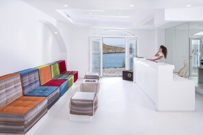 Un hall d’hôtel moderne avec un espace salon, un comptoir d’accueil et une vue sur la mer.