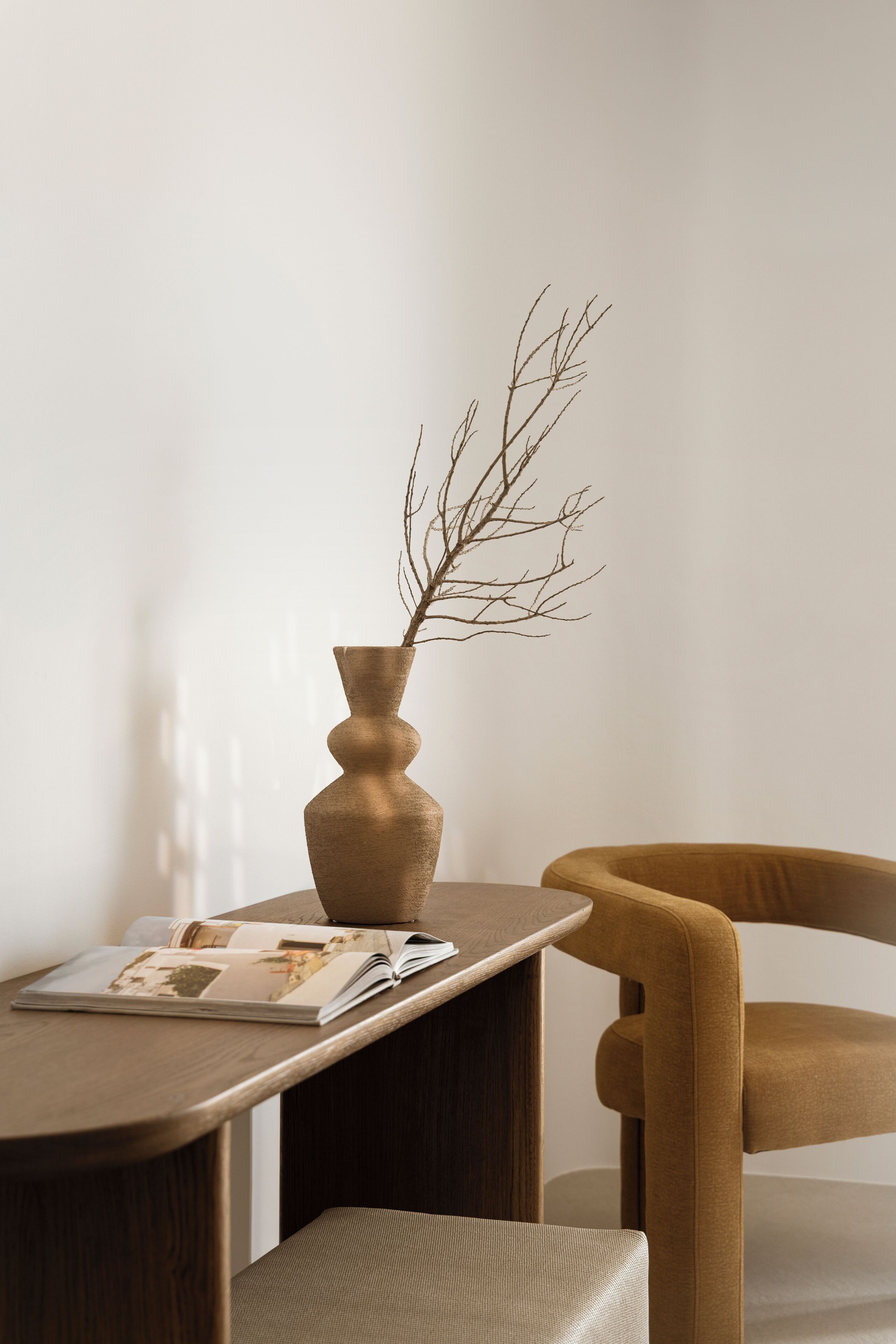 A minimalist room with a wooden table, a brown vase with a branch, and a brown chair.