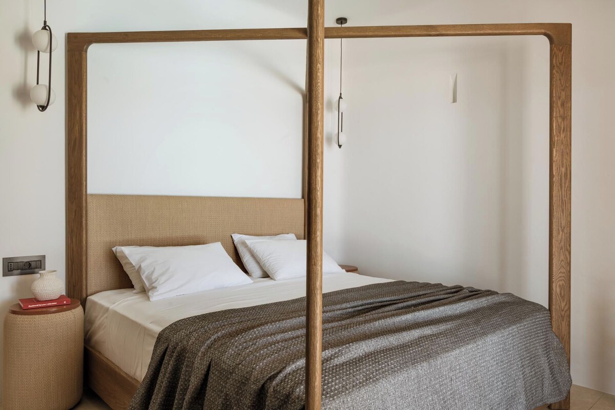 Een bed met houten frame, een geweven hoofdbord en een grijze deken.