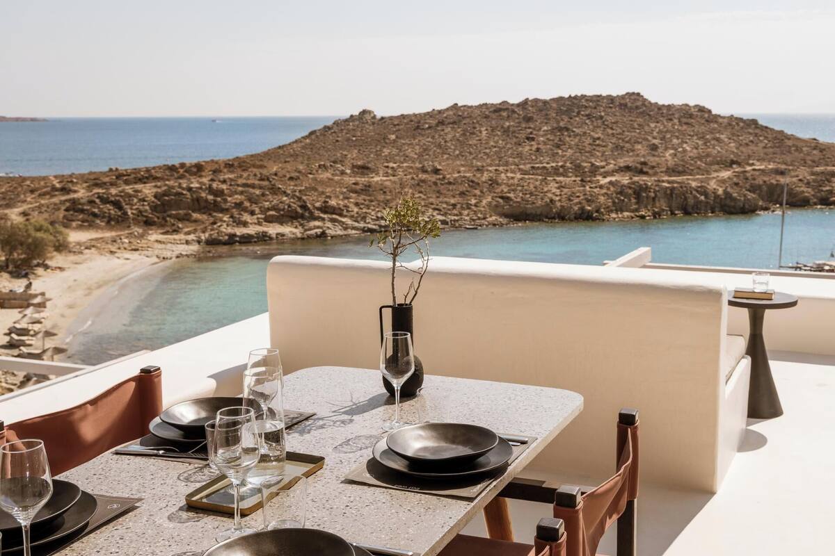 Une table dressée pour le dîner, avec vue sur une côte rocheuse et la mer.