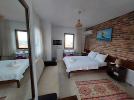 Una habitación de hotel con una cama, una mesita con una planta, un televisor y un ventanal con cortinas.