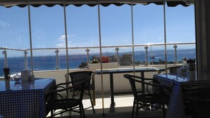 Una terraza con vistas al mar, con manteles a cuadros, sillas de mimbre y una barandilla.