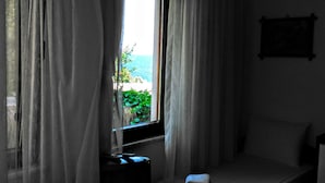 Una habitación con ventana, cortinas, una cama y un cuadro colgado en la pared.