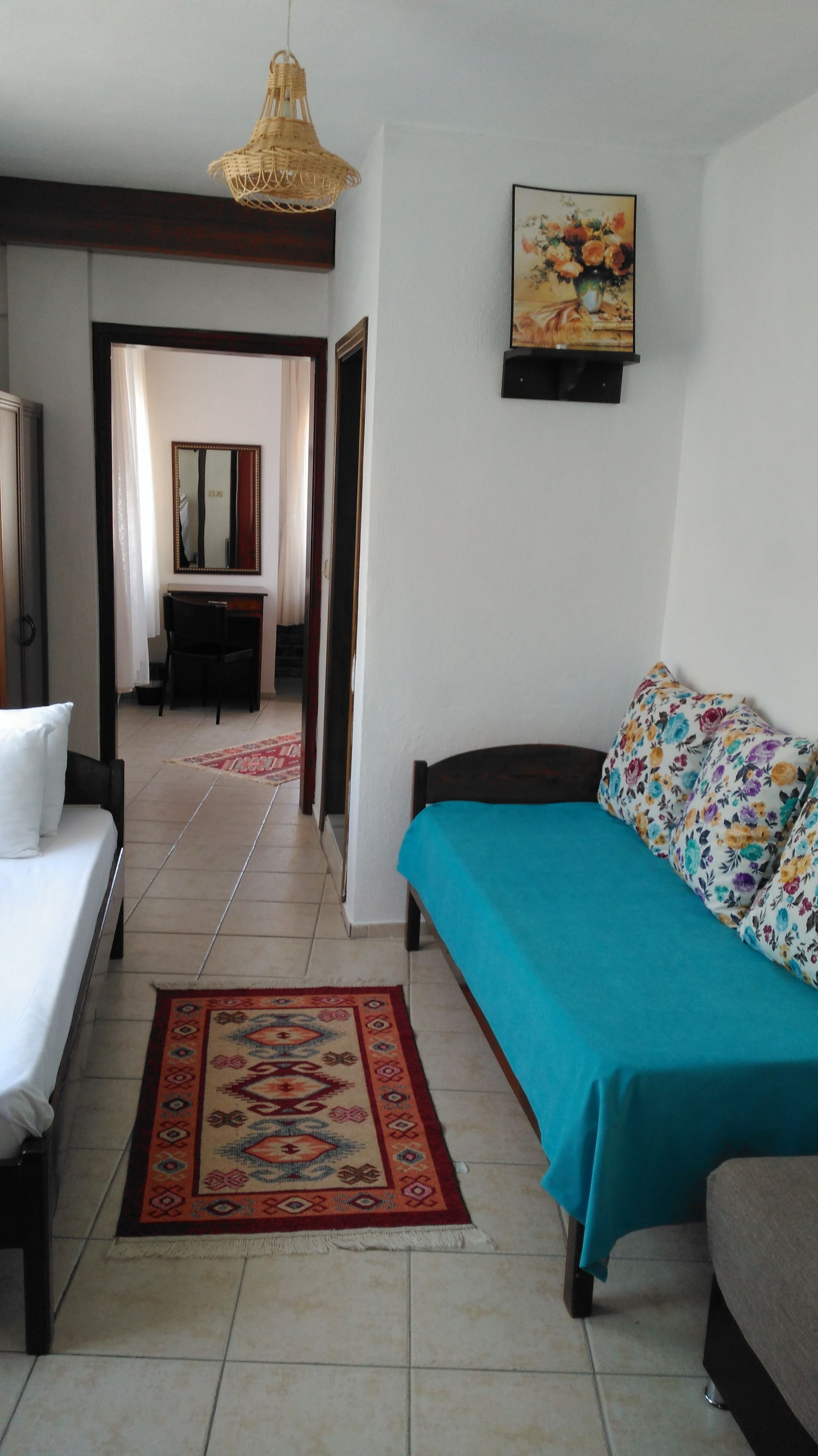 Una habitación con cama, sofá, lámpara colgante, un cuadro y una alfombra estampada.