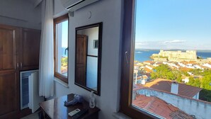 Un dormitorio con un ventanal grande, un escritorio, una silla, una cama con colcha estampada y vistas a un paisaje urbano costero.