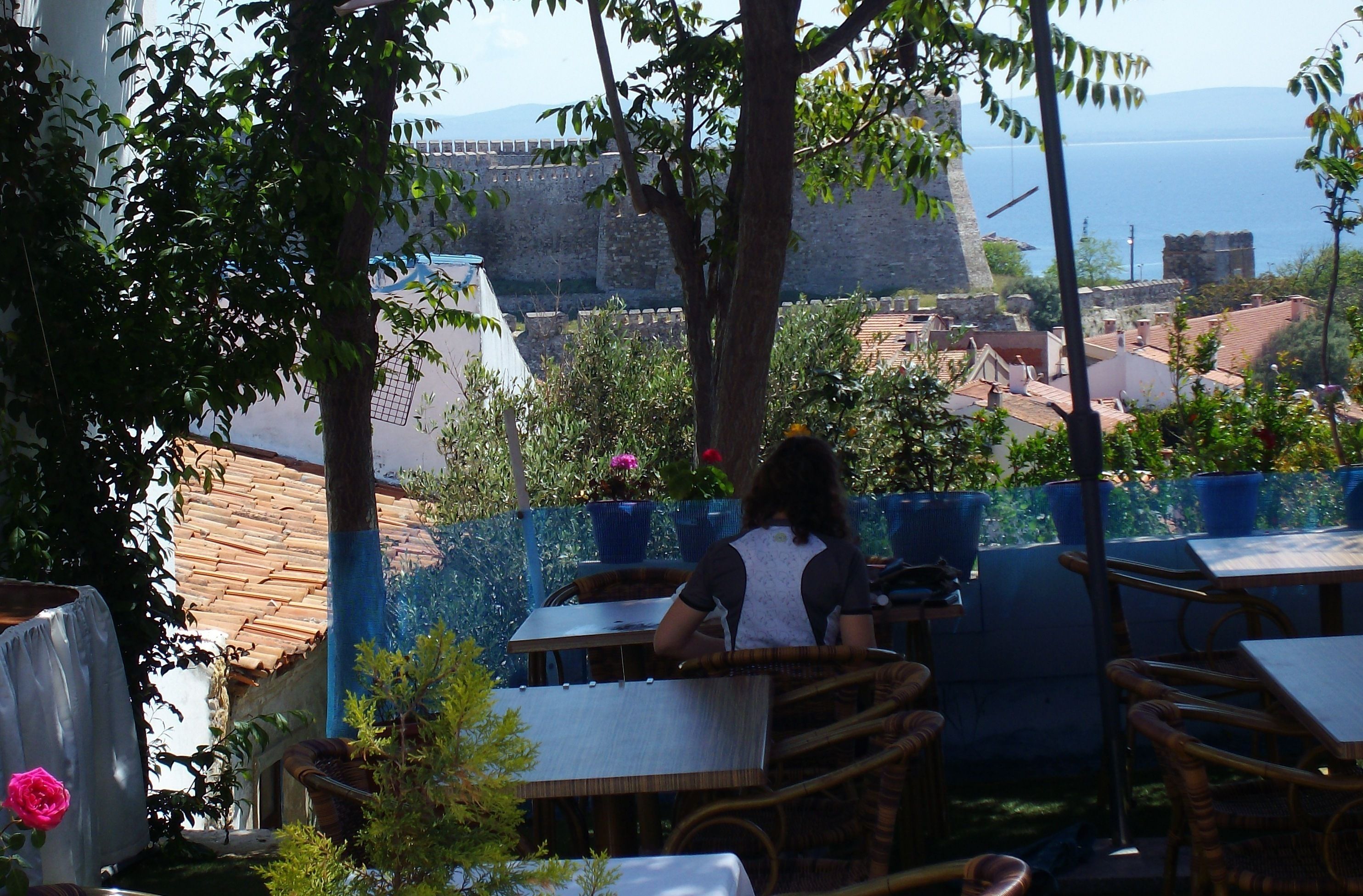 An outdoor seating area with tables and chairs, overlooking a historic fort and the sea.