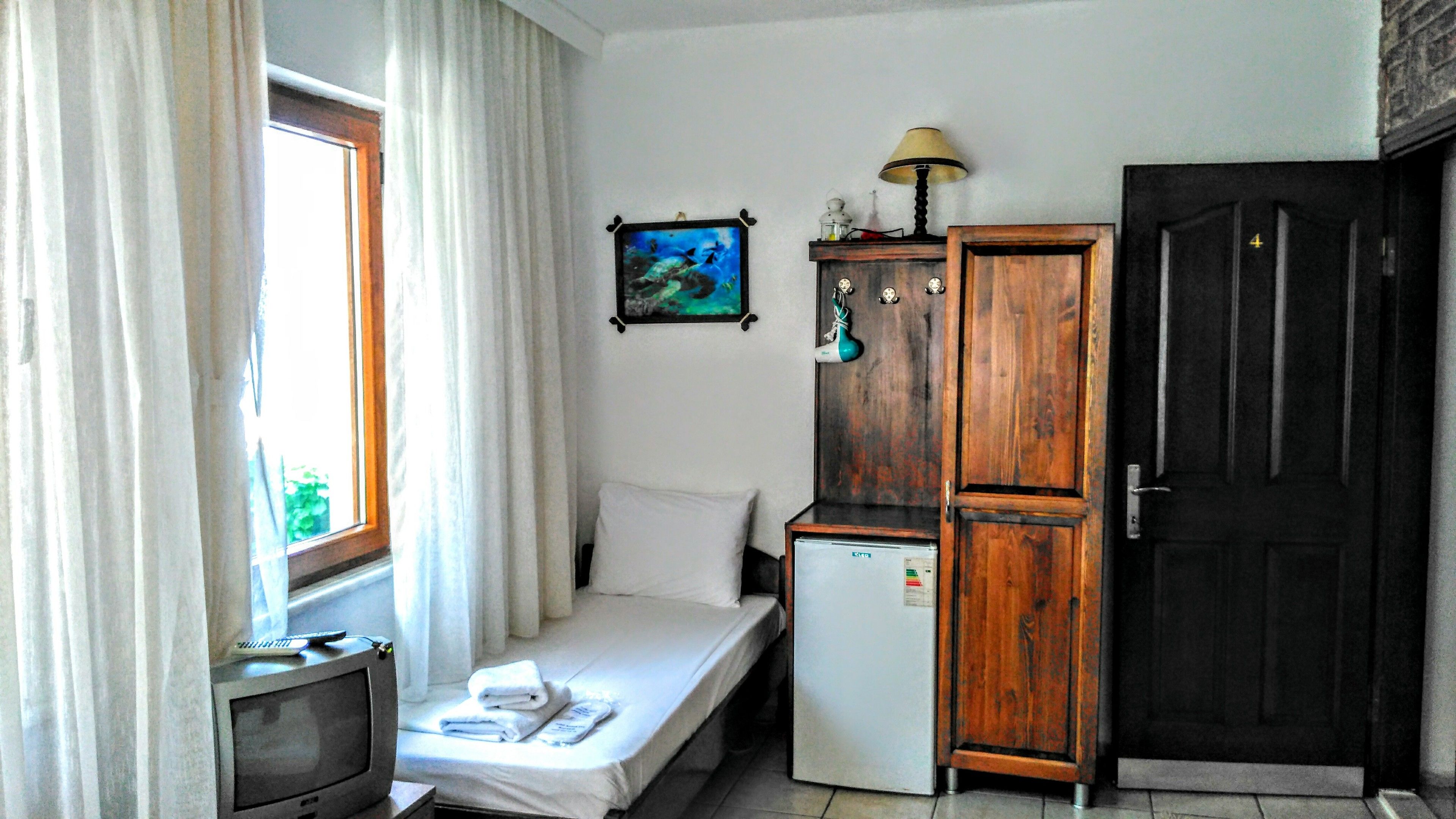 A small room with a bed, a TV, a refrigerator, a wooden cabinet, and a door.