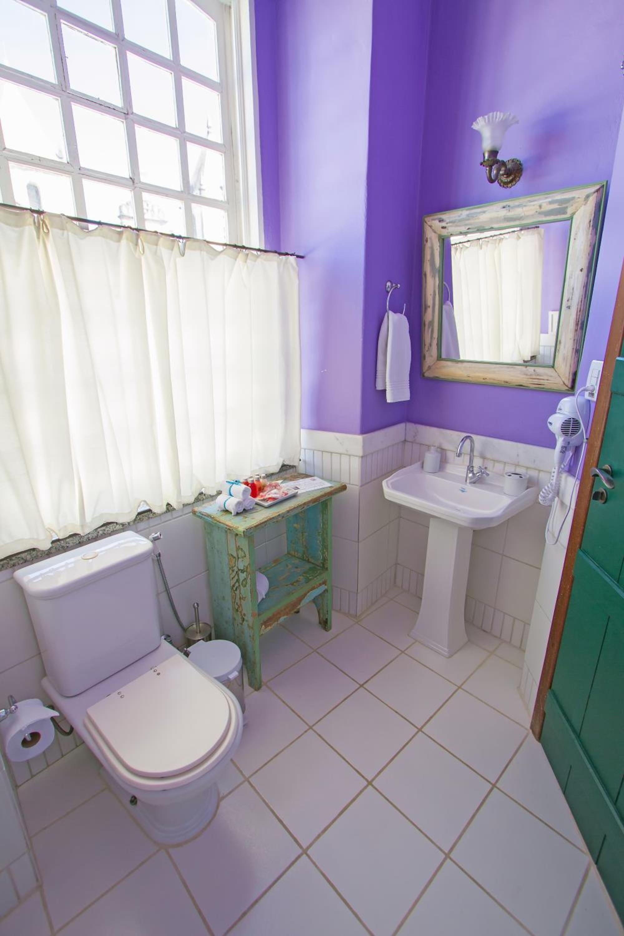 Une salle de bain avec des toilettes, un lavabo et une fenêtre avec des rideaux.