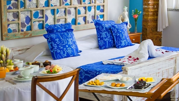 A room with a bed, a table with food, and a decorative wall. - Pousada Solar Dos Deuses (Salvador)