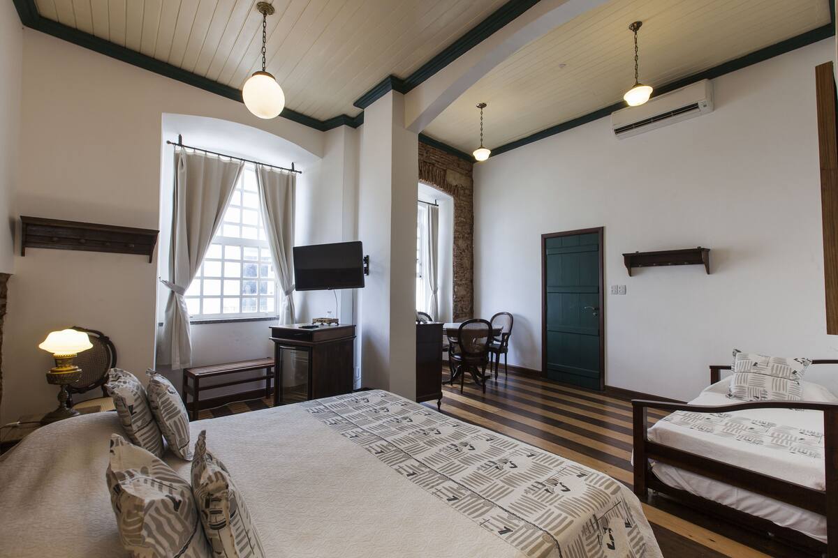 A hotel room with a large bed, a desk with a lamp, a television, and a window with curtains.