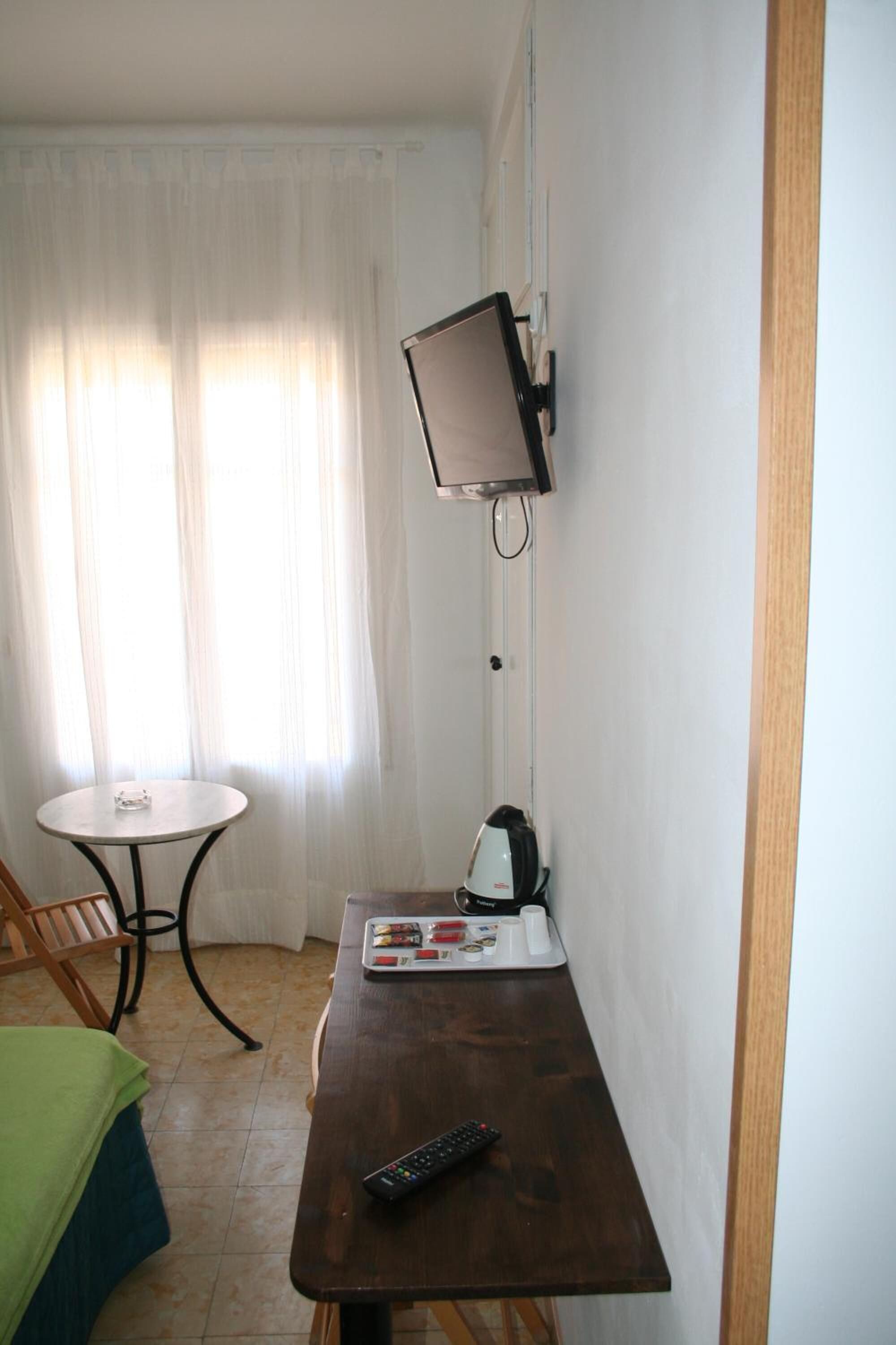 A small room with a wooden table, a wall-mounted TV, a kettle, and a remote control.