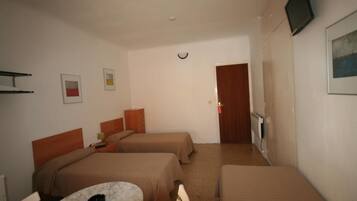 A hotel room with two single beds, a small table, a chair, a TV mounted on the wall, and a door leading to another room.