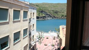 Vista de un edificio costero con múltiples ventanas y balcones que dan a un mar tranquilo y un paisaje montañoso.