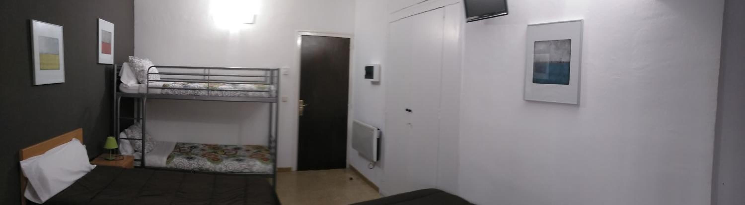 A dormitory room with bunk beds, a desk, a chair, a radiator, and a door.