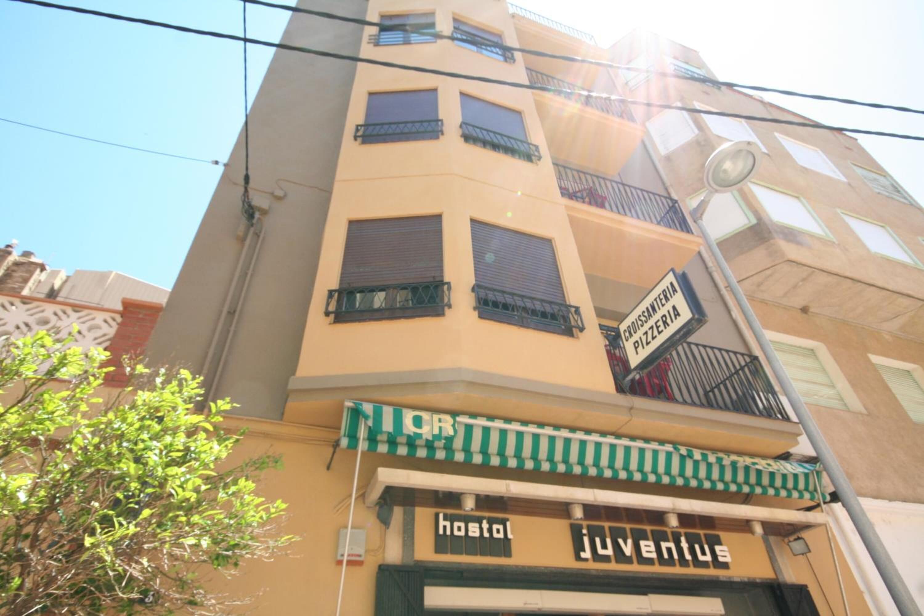 Un bâtiment avec un auvent rayé de vert et de blanc, une enseigne indiquant « hostal Juventus » et une autre indiquant « CROSSWAY PIZZERIA ».