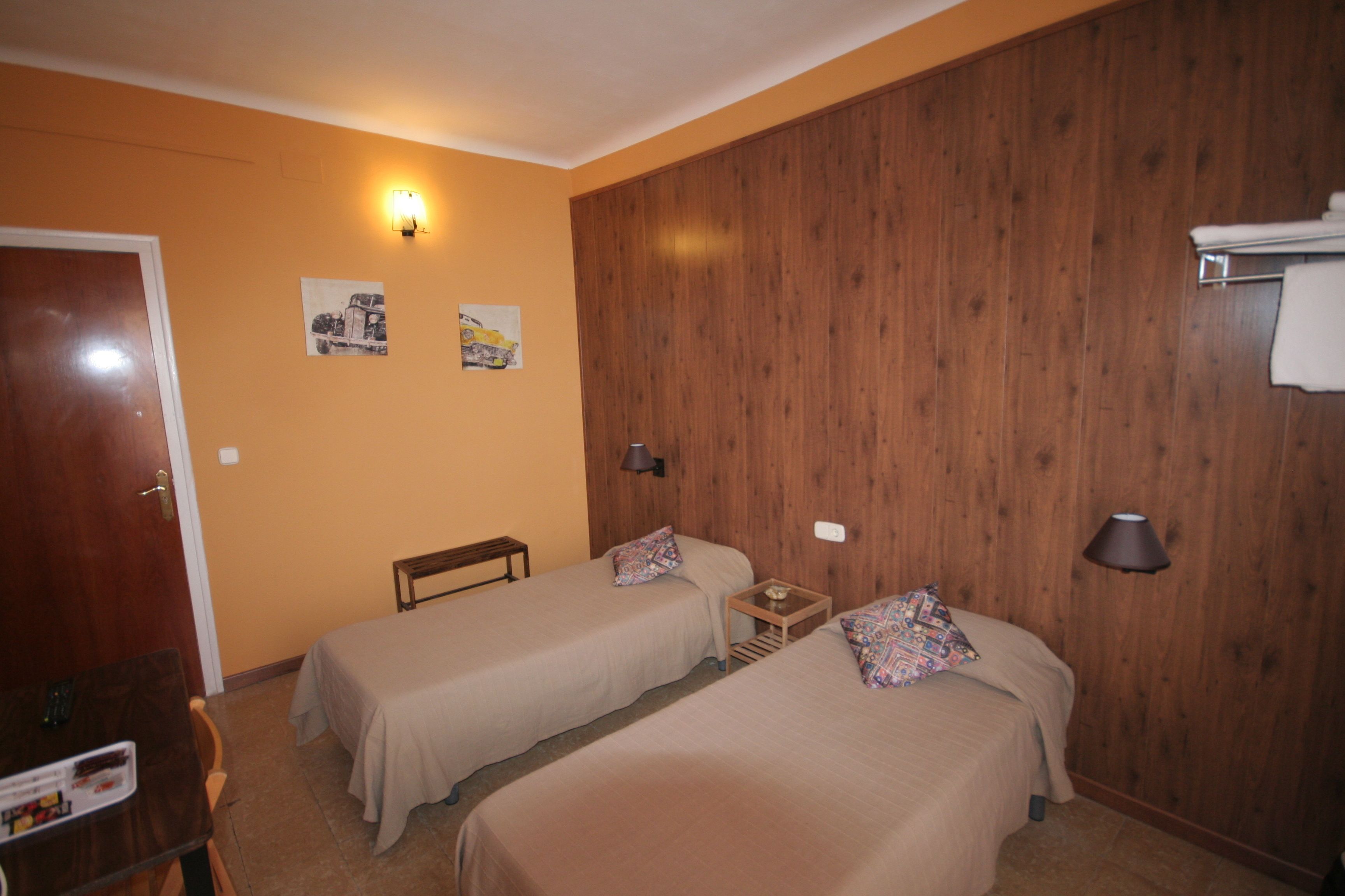Ein Zimmer mit zwei Einzelbetten, einem Holzschrank, einem kleinen Tisch und einer Wandlampe.