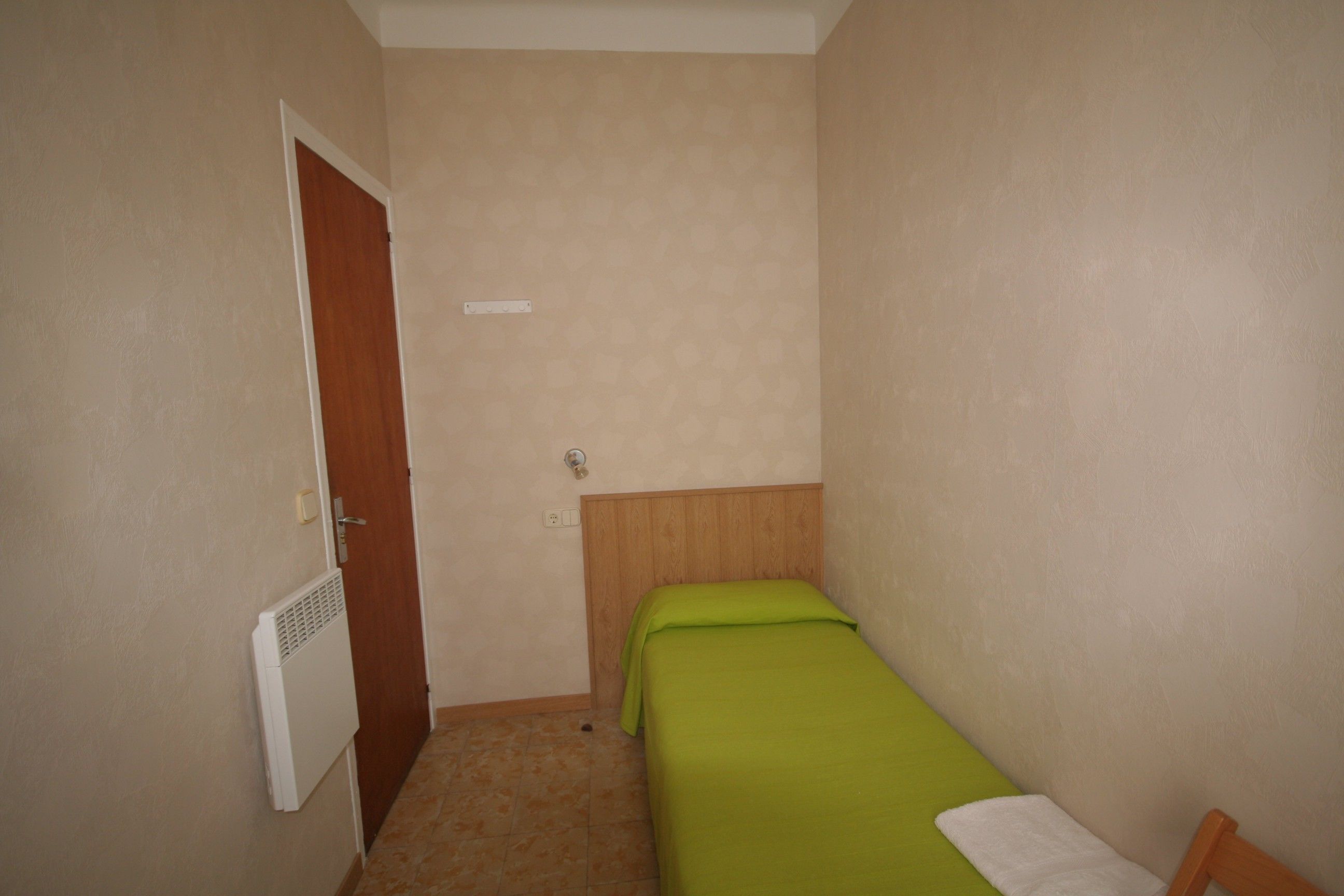 Ein kleiner, schmaler Raum mit einem Bett, einer Heizung und einer Tür.