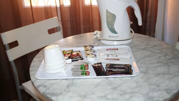 Uma mesa de mármore com uma chaleira branca, um tabuleiro com petiscos variados e uma chávena branca.