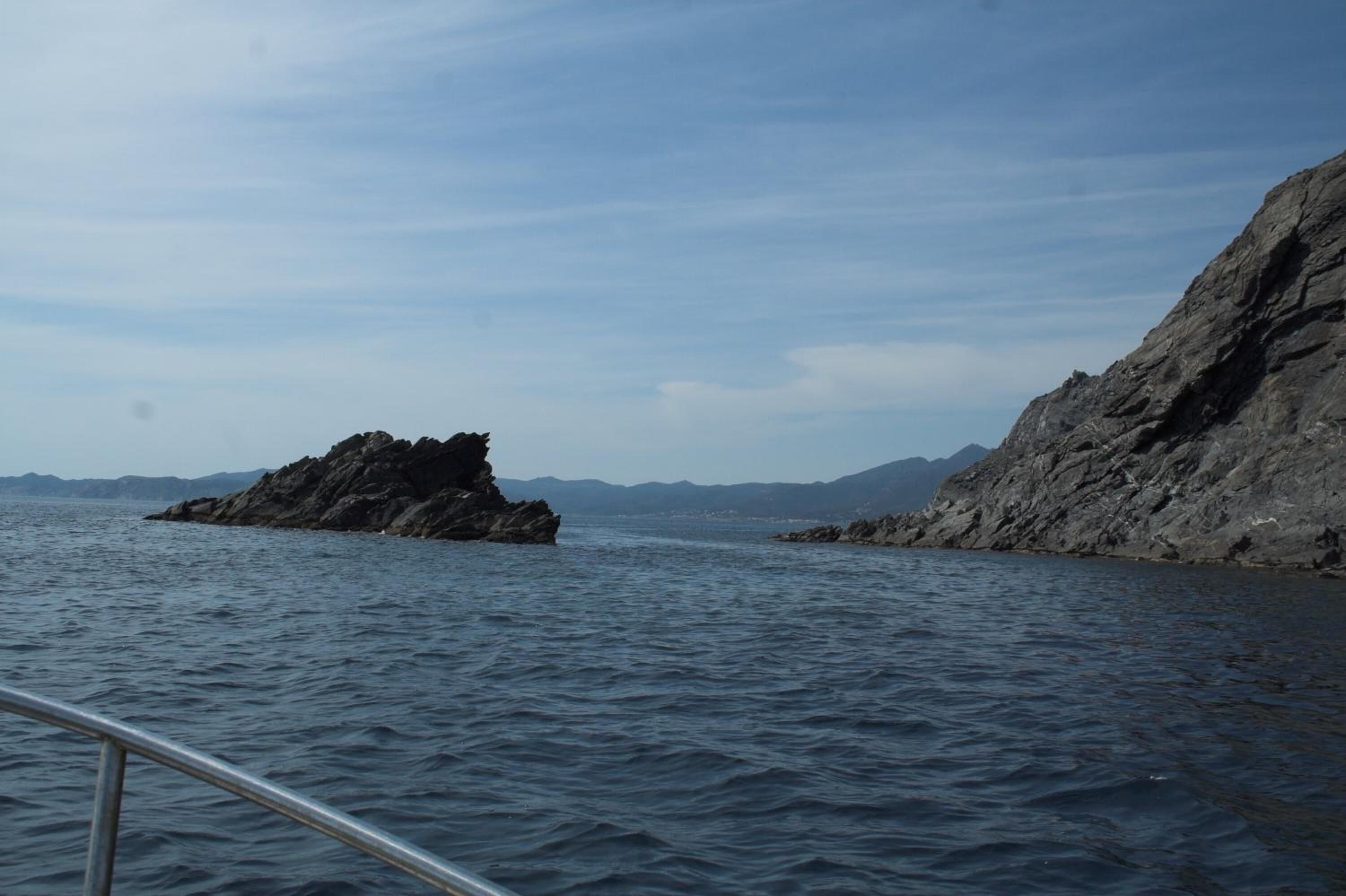 A rocky coastline with calm water and distant mountains.