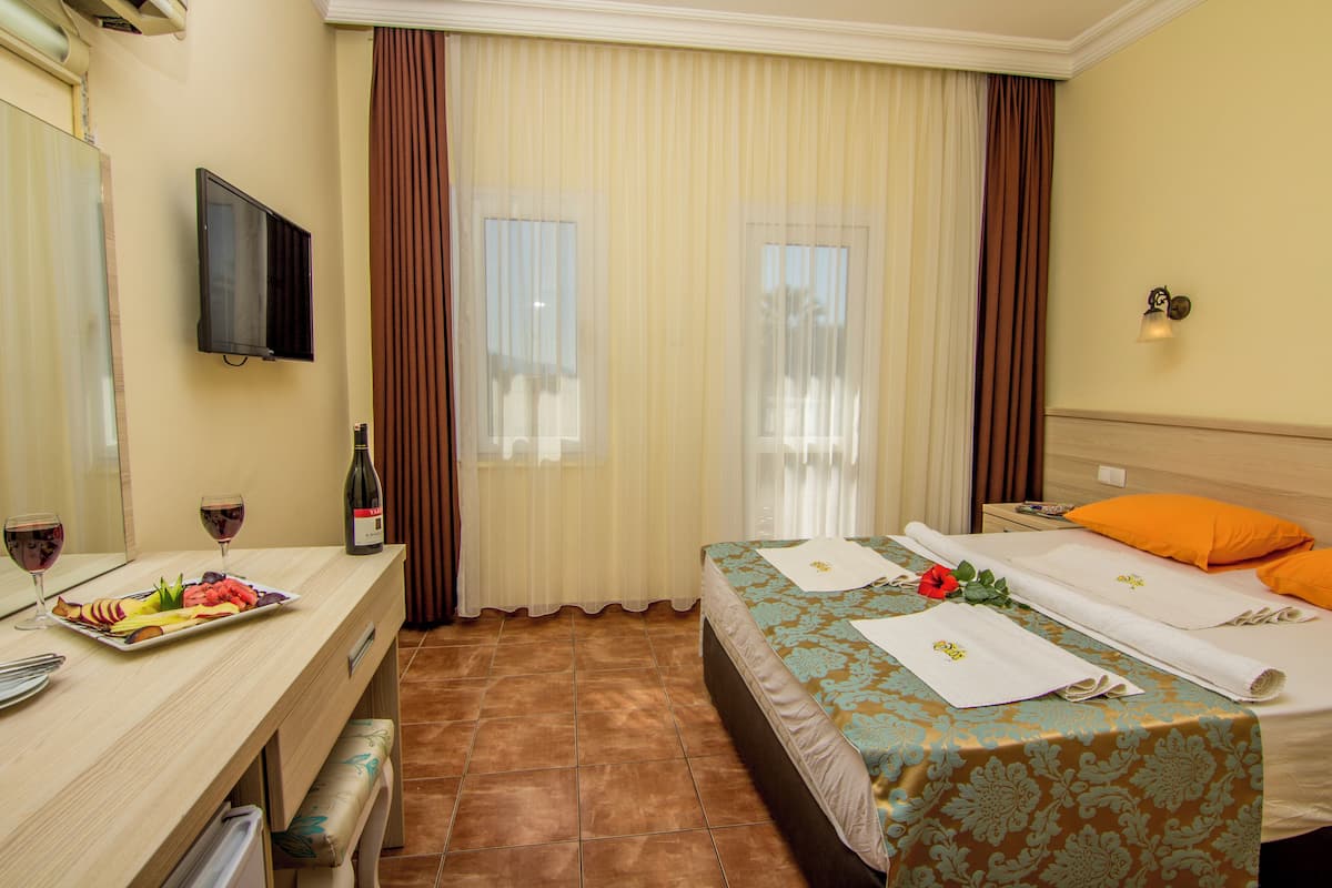 A hotel room with a bed, a desk with a plate of food, a bottle of wine, and a TV on the wall.