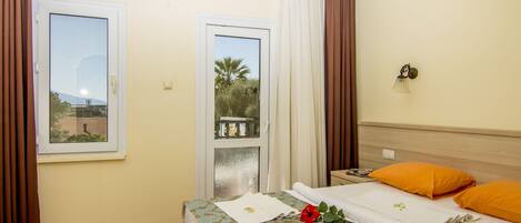 A hotel room with a bed, a window, curtains, and a view of palm trees.