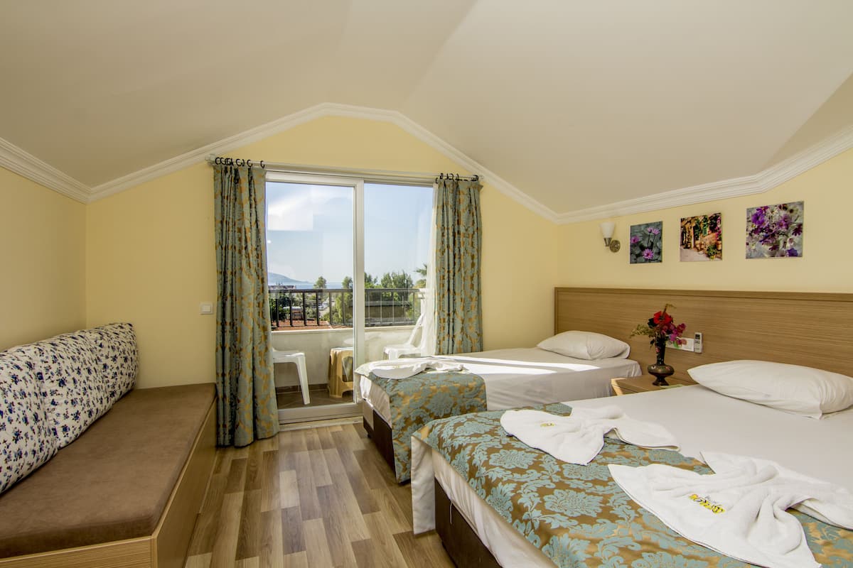 A hotel room with two beds, a sofa, a balcony with curtains, and artwork on the wall.