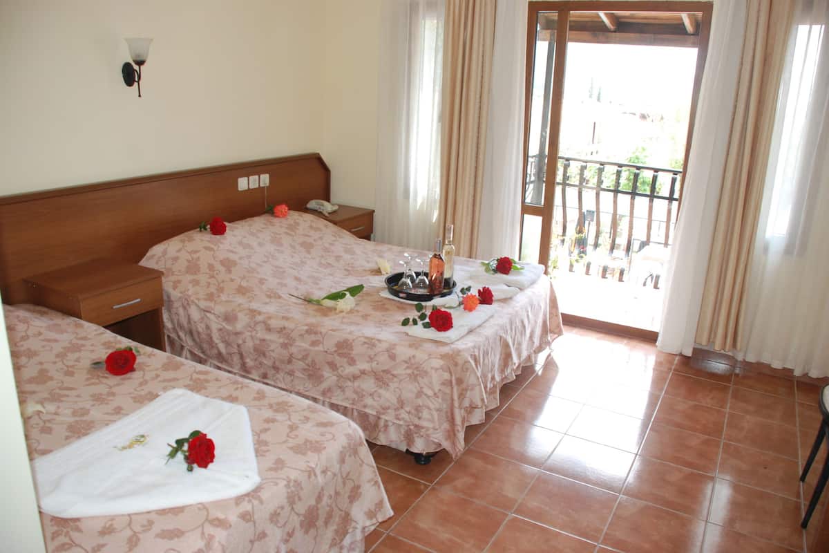 A hotel room with two beds, a wooden headboard, a bedside table with a lamp, and a balcony with a view.