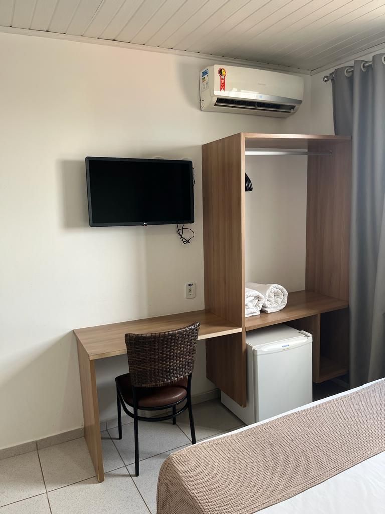 A room with a wooden desk, a television mounted on the wall, a small refrigerator, a chair, and a bed.