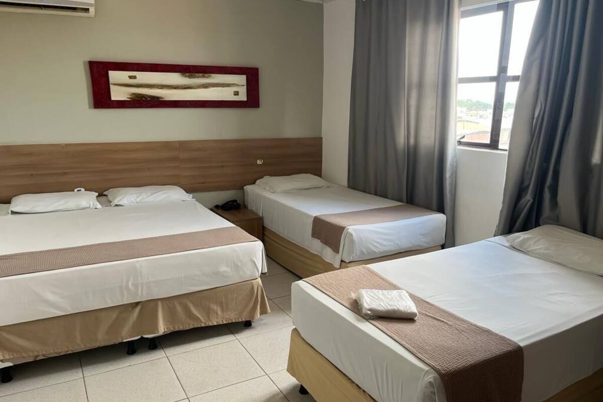Ein Hotelzimmer mit zwei Betten, einem hölzernen Kopfteil, einem gerahmten Bild an der Wand und einem Fenster mit Vorhängen.