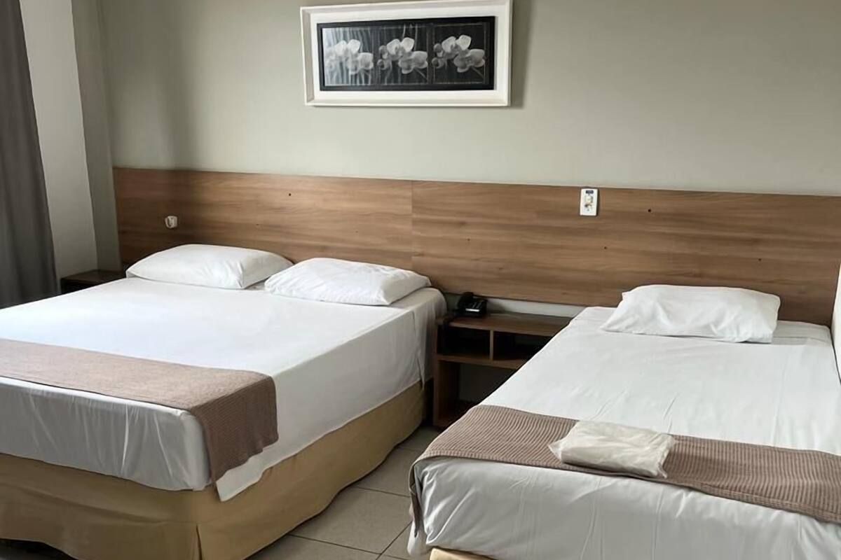 Ein Hotelzimmer mit zwei Betten, einem Holz-Kopfteil, einem gerahmten Bild an der Wand und einem Nachttisch mit einer Lampe.