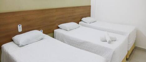 Habitación de hotel con tres camas individuales, cada una con ropa de cama y almohadas blancas. Hay dos cuadros enmarcados en la pared sobre las camas.