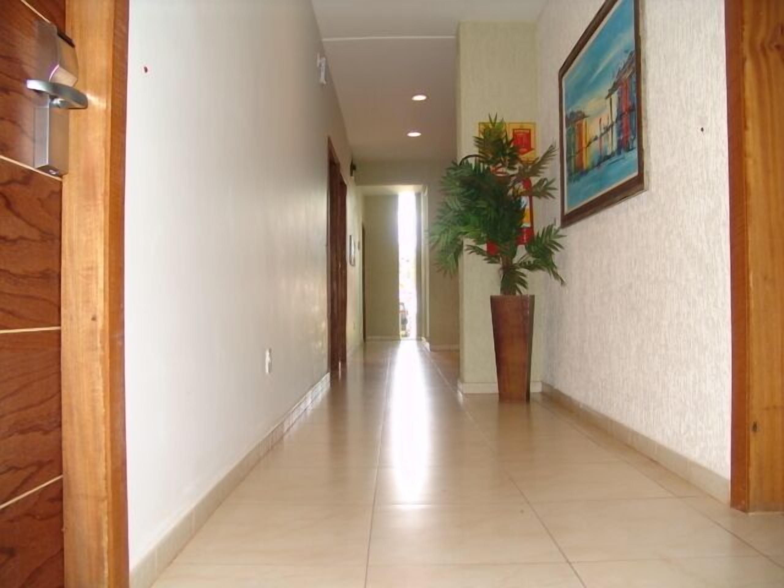 A hallway with a wooden floor, a potted plant, and a painting on the wall.
