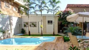 A swimming pool with a wooden deck, surrounded by palm trees and plants. - Ecos Conforto (Porto Velho)